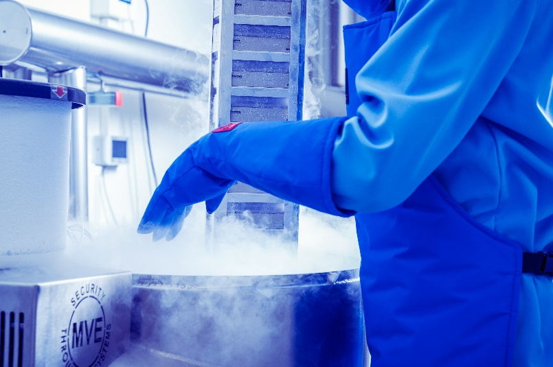 Laboratoriossa vaaleansinipukuinen työntekijä nostaa räkkitelinettä nestetyppiastiasta.